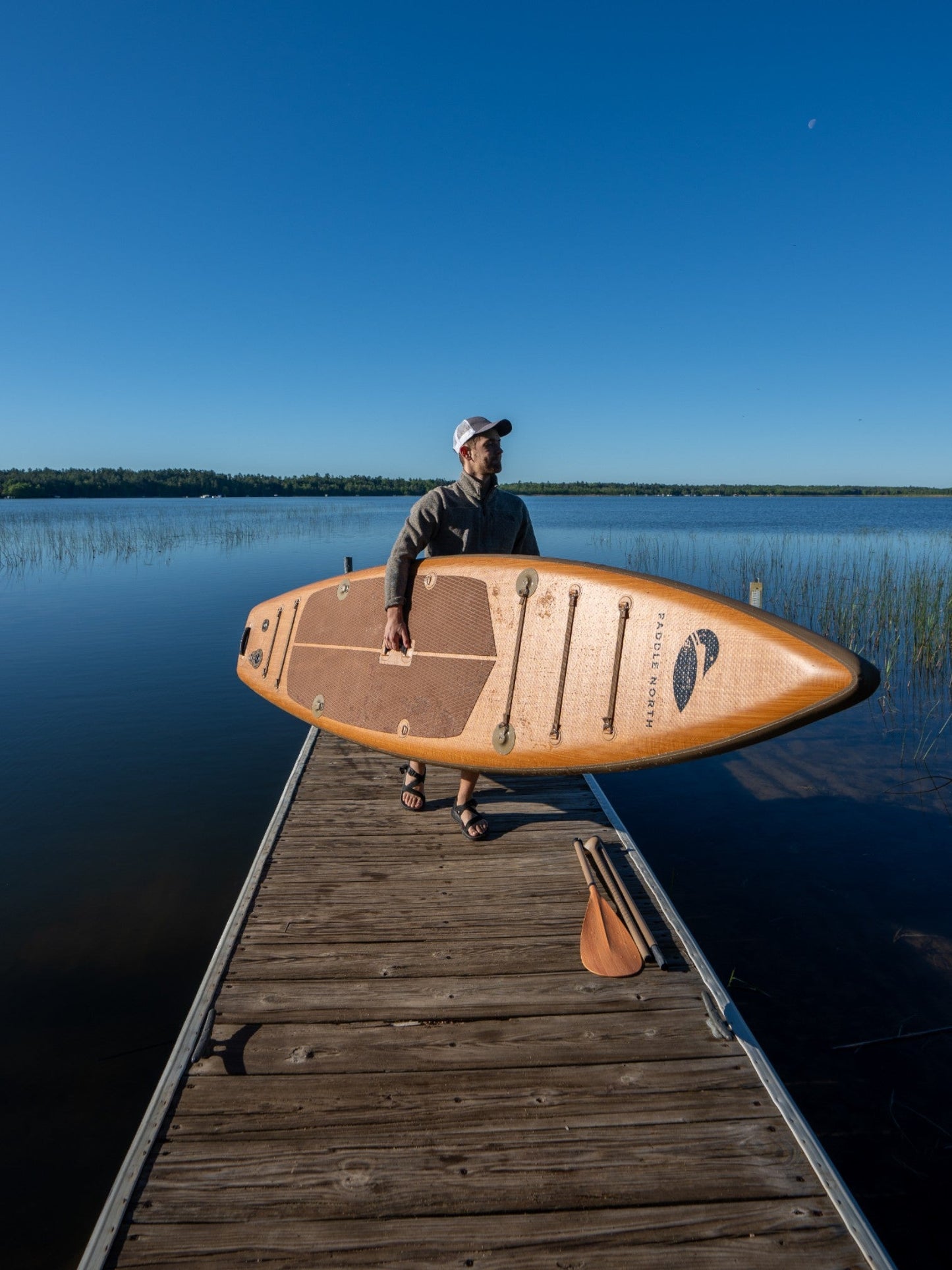 Person carrying a paddle board up a dock.