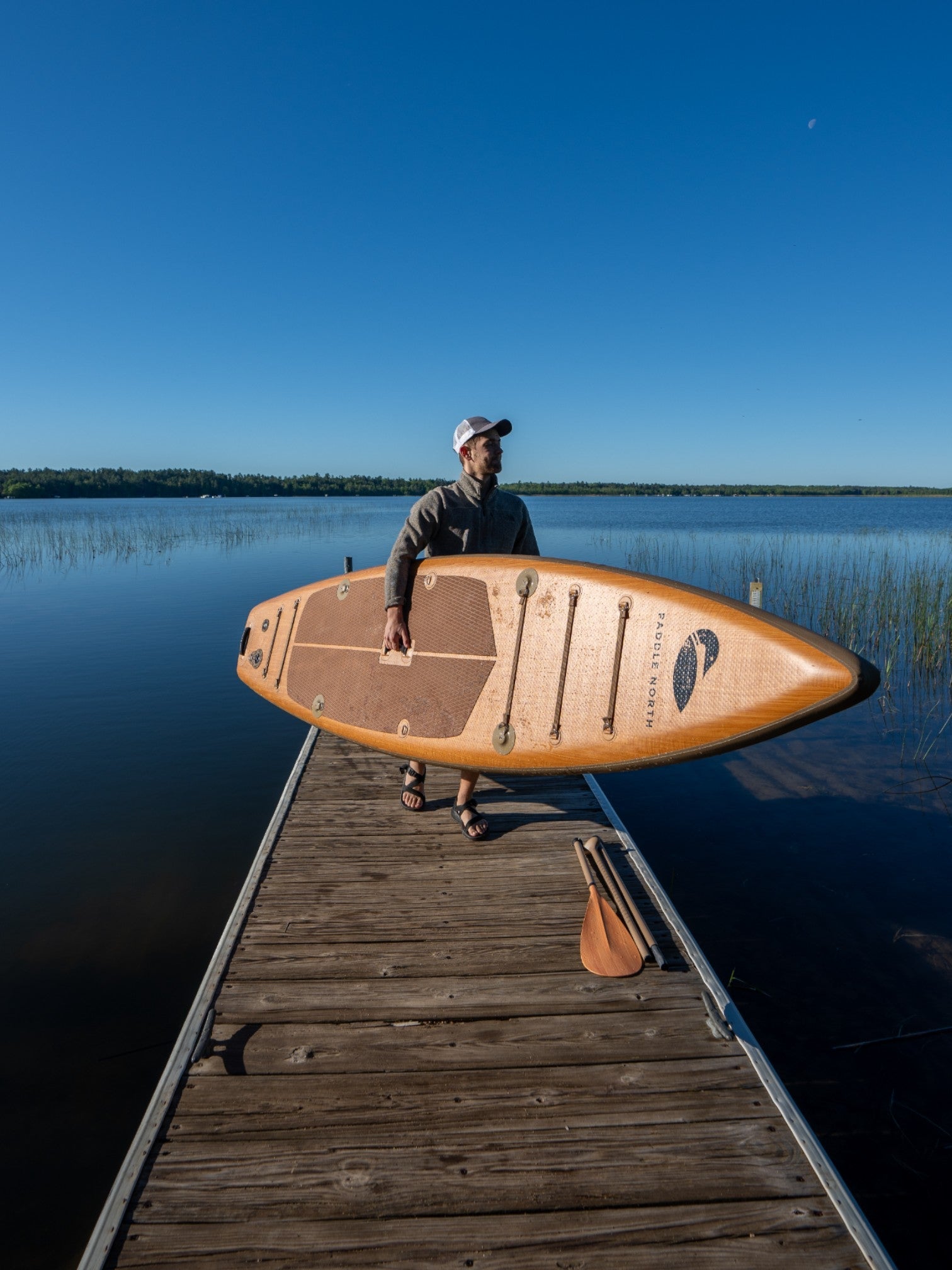 Person carrying a paddle board up a dock.