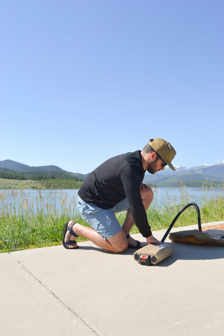 Man inflating his paddle board with a tan inflator by the lake.