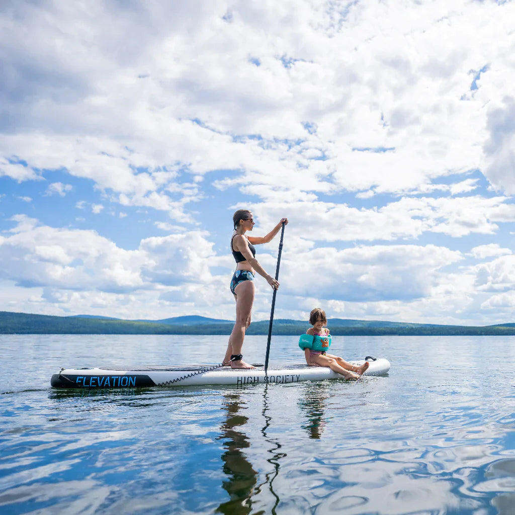 Woman paddling in a lake with a young girl sitting on the front of the board