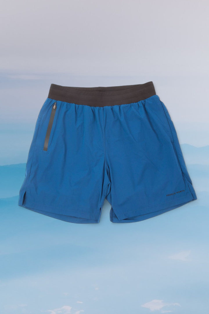 Blue shorts with a black elastic waistband against a blue wavy background.