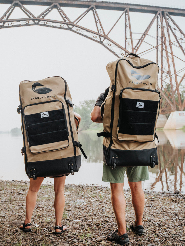 Two people standing away from us wearing a paddle north kayak bag as a backpack.