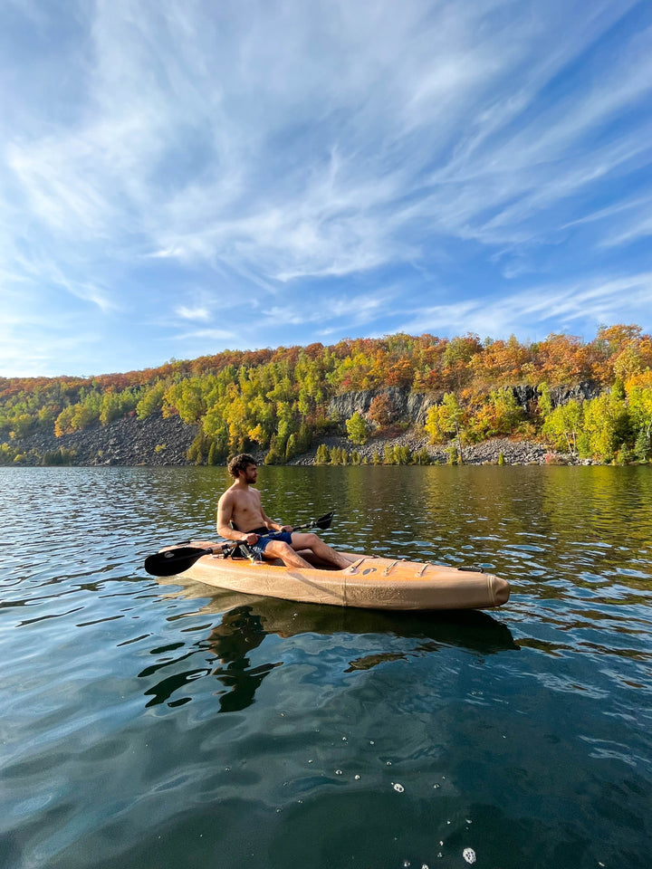 Person kayaking in water with trees in the background.