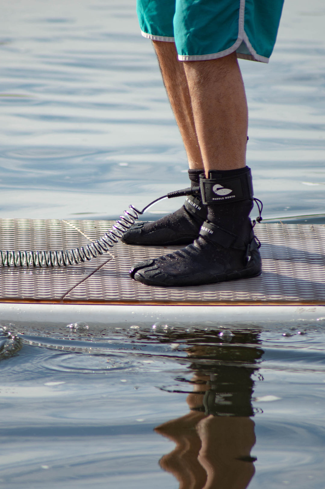 Paddle board accessories: person standing on a paddle board in the water wearing water shoes and Paddle North SUP Leash attached to their ankle.