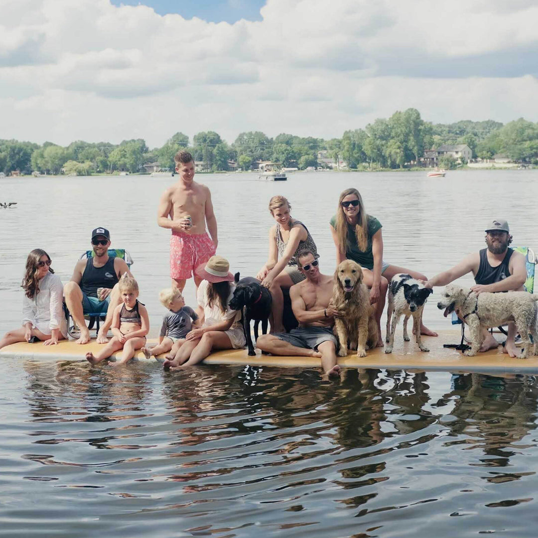 Several people and a few dogs all sitting on an inflatable dock in the water.