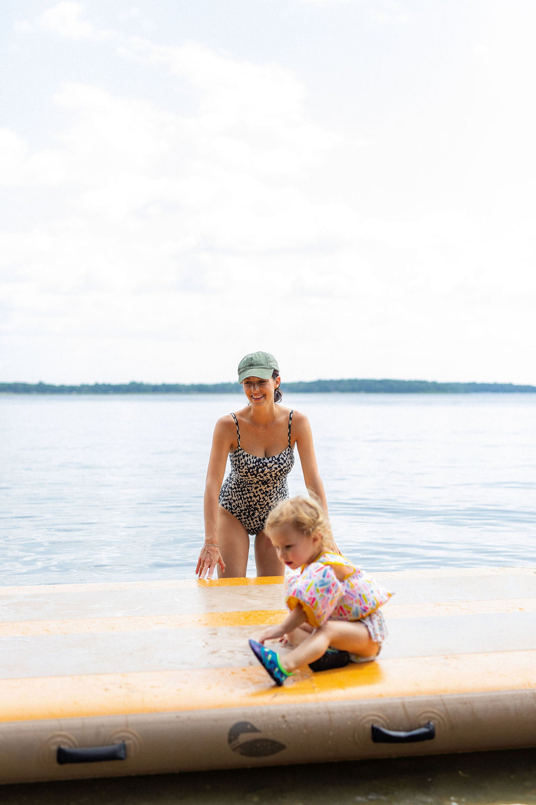 Woman stand in the water next to a child sitting on an inflatable dock.