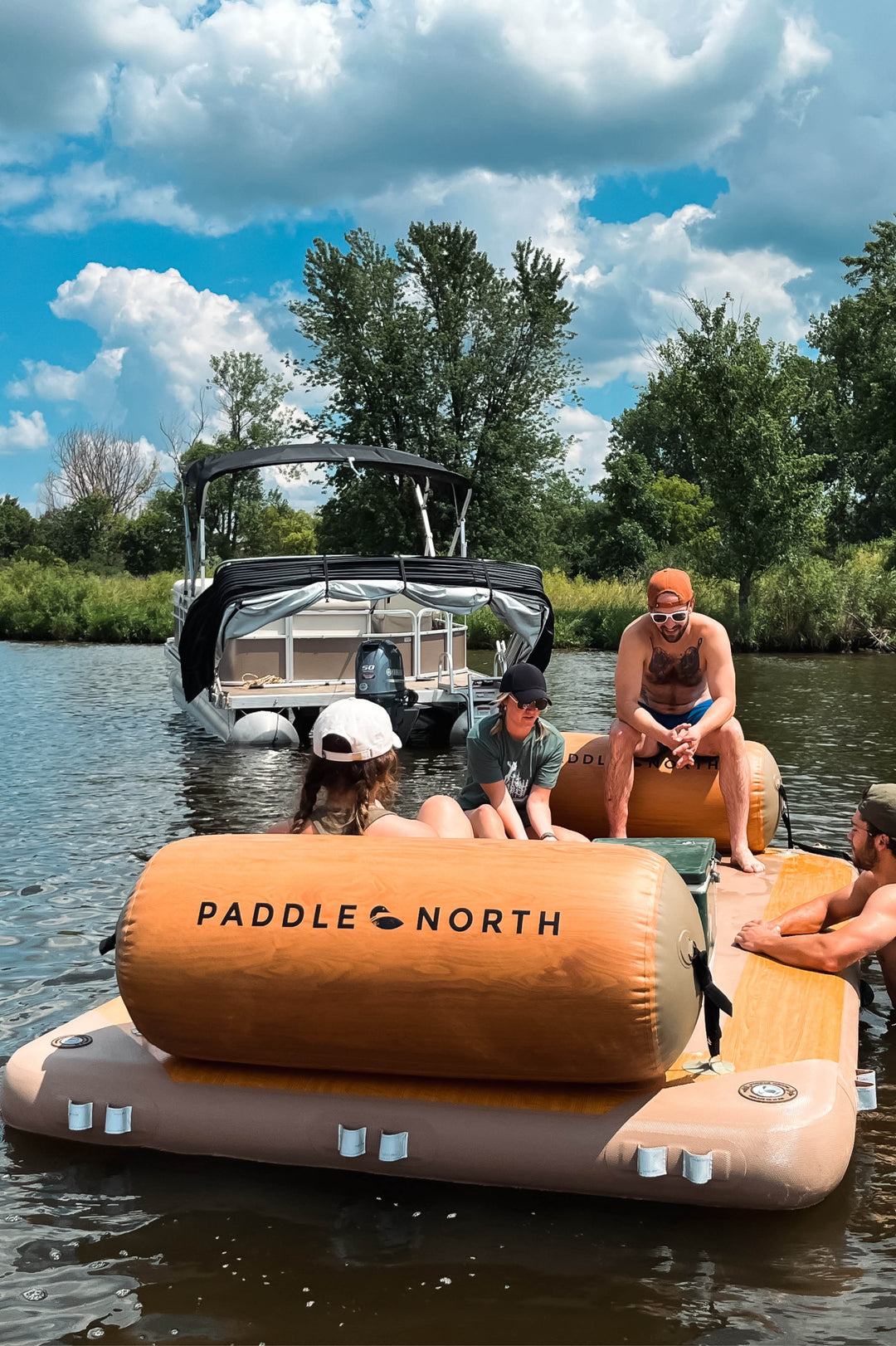 People sitting on an inflatable dock in the water with two lake logs attached to it.