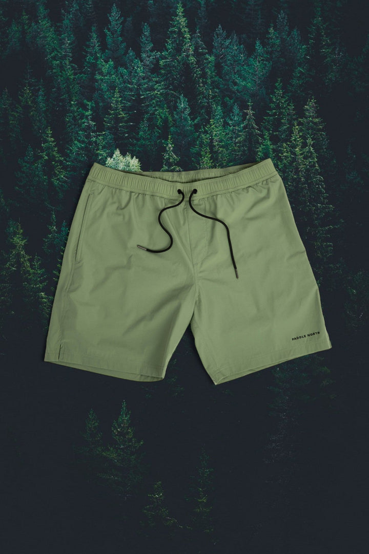 Pair of green shorts against an evergreen tree background.