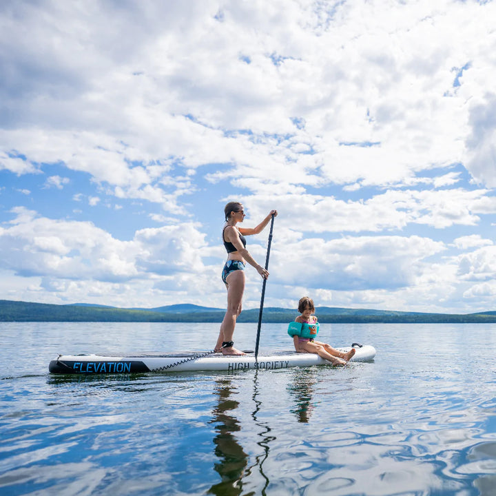 Woman paddling in a lake with a young girl sitting on the front of the board